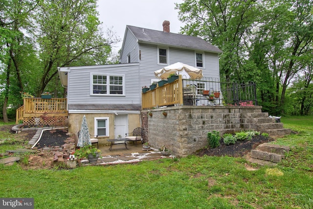back of house featuring a patio area, a deck, a chimney, and a lawn