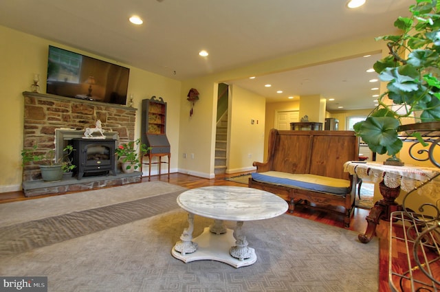 living area featuring recessed lighting, wood finished floors, a wood stove, stairs, and baseboards