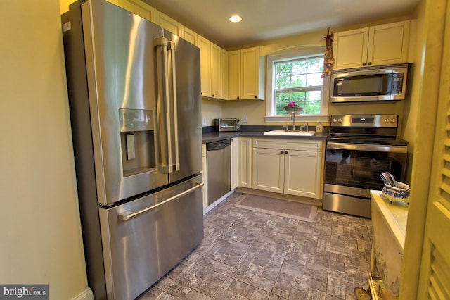 kitchen featuring appliances with stainless steel finishes, a sink, dark countertops, recessed lighting, and brick patterned floors