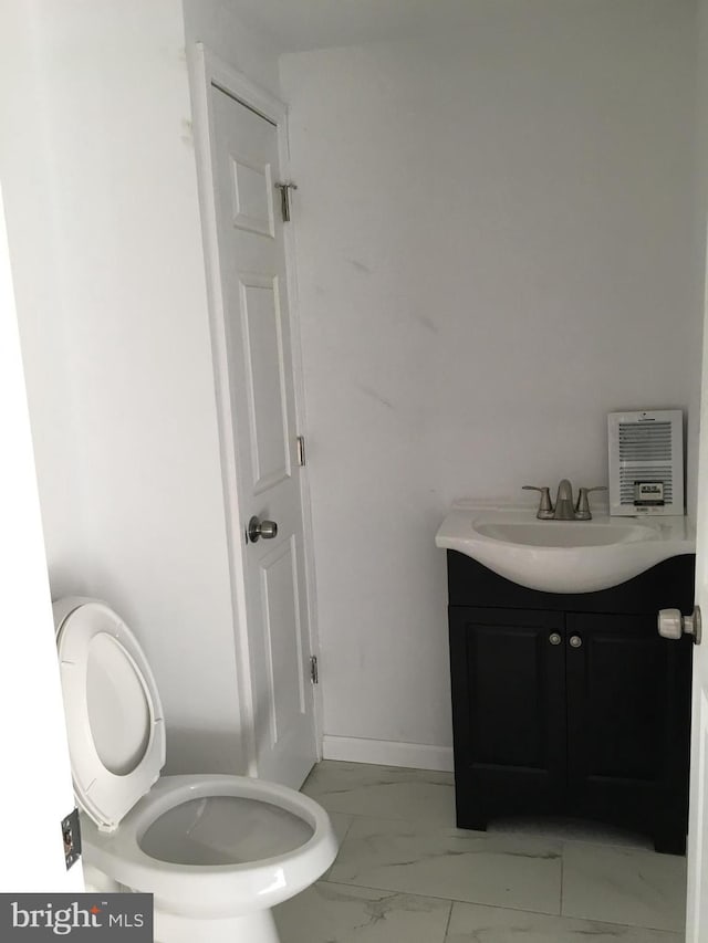 half bath with marble look tiles, vanity, heating unit, and toilet
