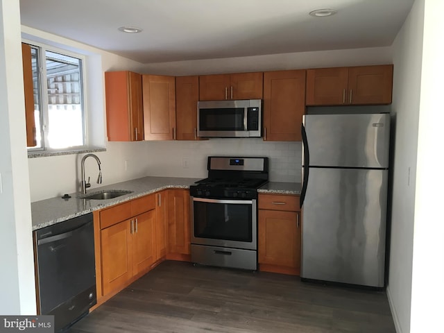 kitchen with appliances with stainless steel finishes, a sink, light stone countertops, dark wood-style floors, and backsplash