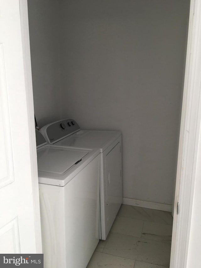 laundry area featuring separate washer and dryer, baseboards, and light marble finish flooring