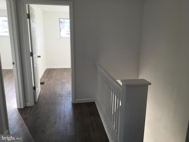 hall with dark wood-style floors, baseboards, and an upstairs landing