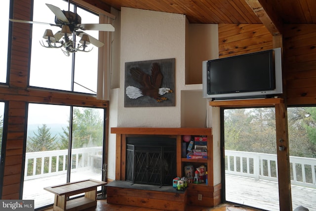 living room featuring wood ceiling, plenty of natural light, ceiling fan, a fireplace with raised hearth, and wooden walls