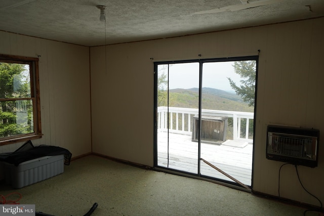 spare room with heating unit, a textured ceiling, a mountain view, wooden walls, and baseboards