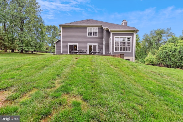 rear view of property with a chimney and a lawn