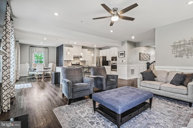 living area featuring ceiling fan, wainscoting, dark wood-type flooring, recessed lighting, and a decorative wall