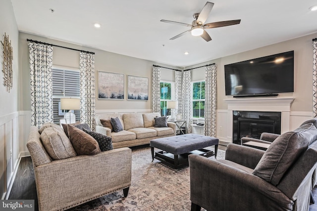 living room with ceiling fan, wood finished floors, wainscoting, a glass covered fireplace, and recessed lighting