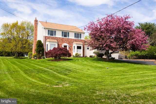 colonial house with a chimney, a front lawn, asphalt driveway, and brick siding