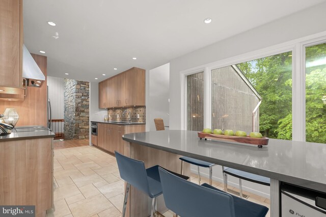 kitchen with a sink, backsplash, dark countertops, recessed lighting, and brown cabinets