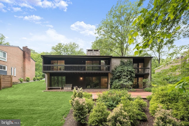 back of property with a balcony, a yard, and a chimney