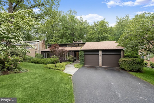 mid-century modern home featuring a front yard, an attached garage, asphalt driveway, and roof with shingles