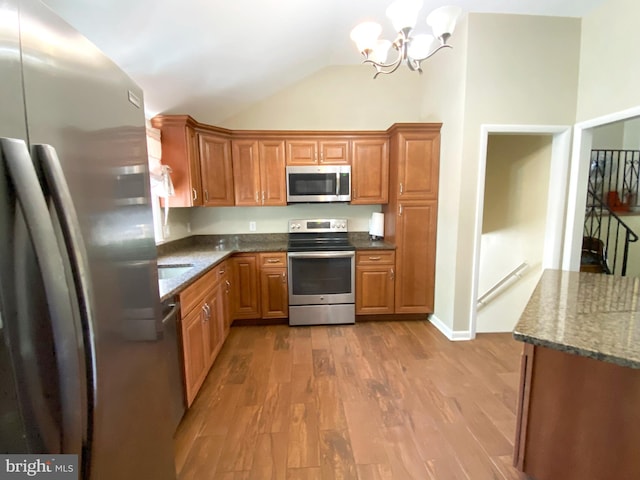 kitchen with stainless steel appliances, vaulted ceiling, brown cabinets, a chandelier, and wood finished floors