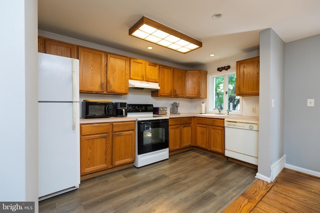 kitchen with white appliances, under cabinet range hood, a sink, brown cabinetry, and light countertops