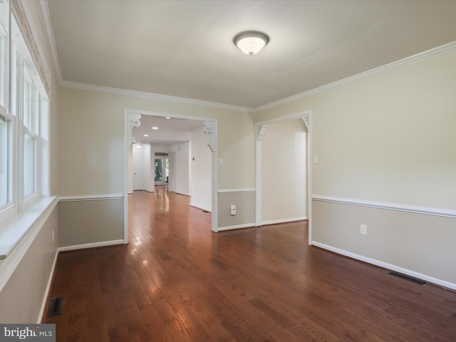 empty room featuring plenty of natural light, wood finished floors, ornamental molding, and baseboards