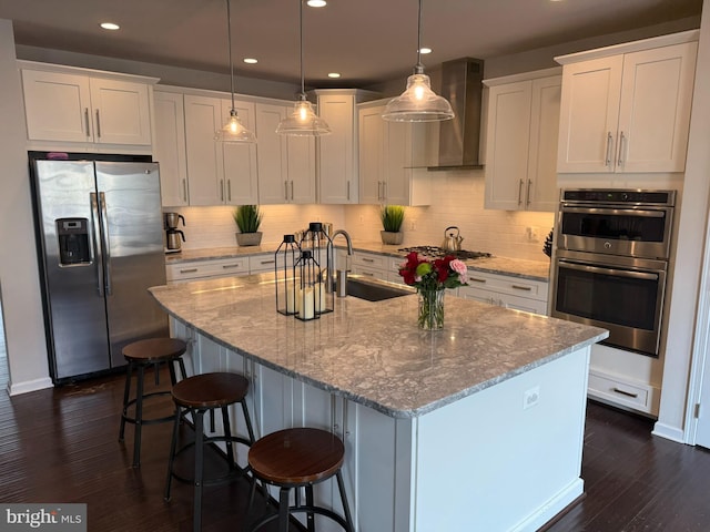 kitchen featuring appliances with stainless steel finishes, a sink, white cabinetry, wall chimney range hood, and dark wood-style floors
