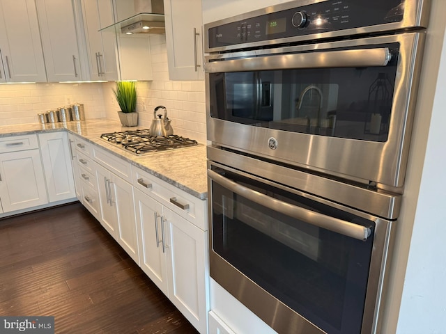 kitchen featuring appliances with stainless steel finishes, exhaust hood, white cabinets, tasteful backsplash, and dark wood-type flooring