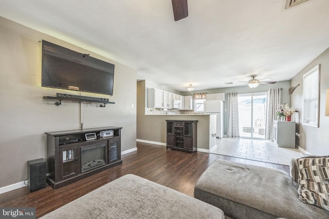 living room with a ceiling fan, baseboards, and dark wood-style flooring