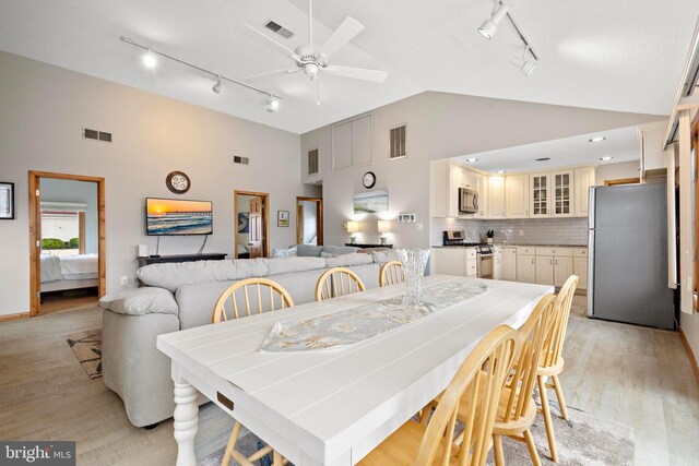 dining space with track lighting, high vaulted ceiling, light wood-type flooring, and ceiling fan