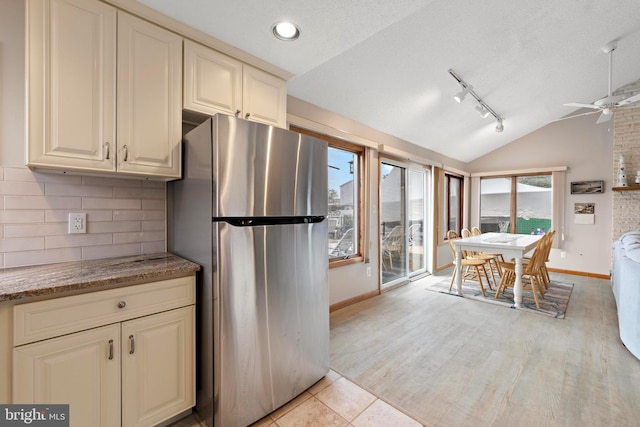 kitchen with freestanding refrigerator, vaulted ceiling, baseboards, cream cabinetry, and tasteful backsplash