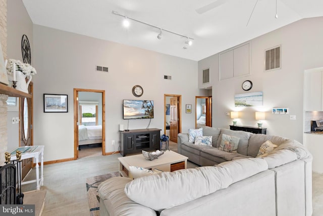 living area featuring a high ceiling, a ceiling fan, baseboards, rail lighting, and light colored carpet