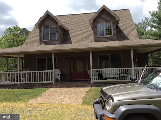 country-style home featuring covered porch, a front lawn, and roof with shingles