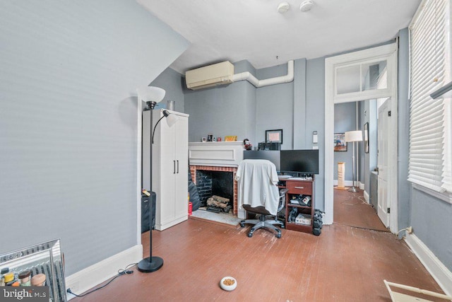 home office featuring a wall mounted air conditioner, wood finished floors, baseboards, and a brick fireplace