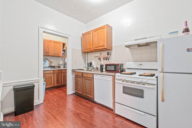kitchen with white appliances, dark wood-style floors, decorative backsplash, light countertops, and under cabinet range hood