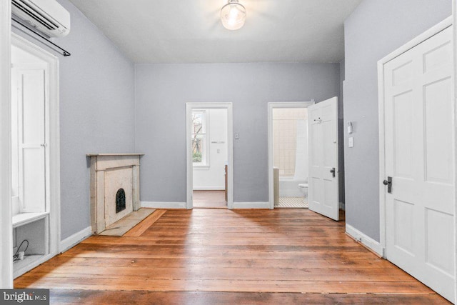 unfurnished living room with an AC wall unit, wood-type flooring, and baseboards