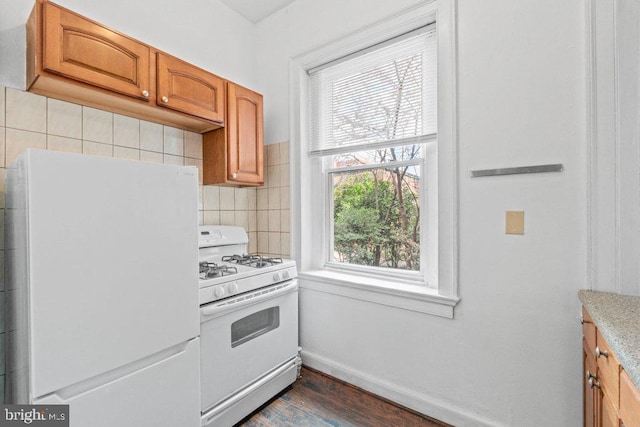 kitchen with white appliances, dark wood finished floors, backsplash, baseboards, and brown cabinets