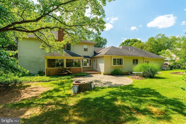 back of house with a patio, an outdoor fire pit, a yard, brick siding, and a chimney