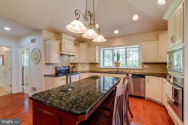 kitchen with appliances with stainless steel finishes, a sink, custom range hood, a kitchen island, and light wood finished floors