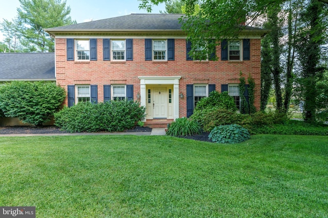 view of front of property with a front lawn, brick siding, and roof with shingles