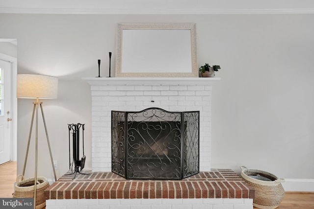 detailed view of a brick fireplace, ornamental molding, wood finished floors, and baseboards