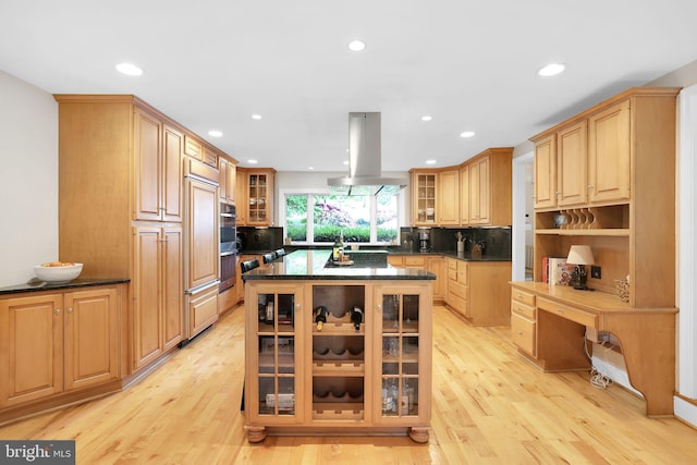 kitchen with island range hood, light wood-style flooring, recessed lighting, backsplash, and glass insert cabinets