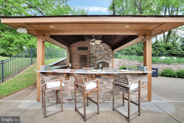 view of patio / terrace featuring fence, an outdoor stone fireplace, and a ceiling fan