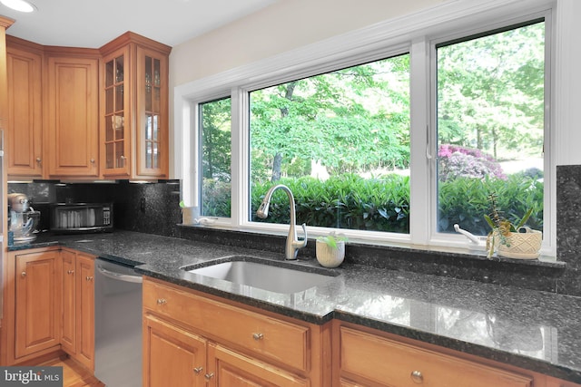 kitchen with stainless steel dishwasher, a sink, dark stone counters, and decorative backsplash