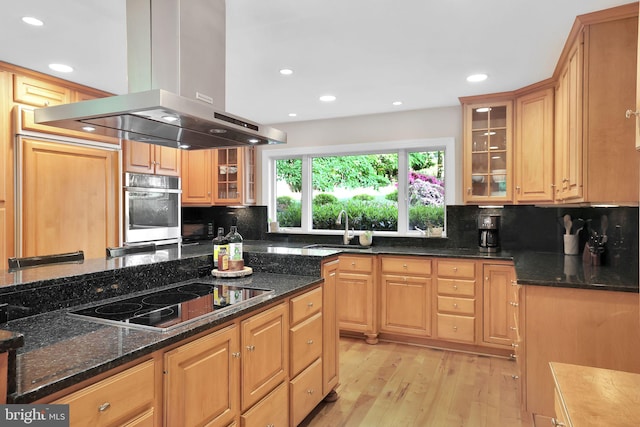 kitchen with island exhaust hood, black electric stovetop, stainless steel oven, a sink, and light wood-style flooring