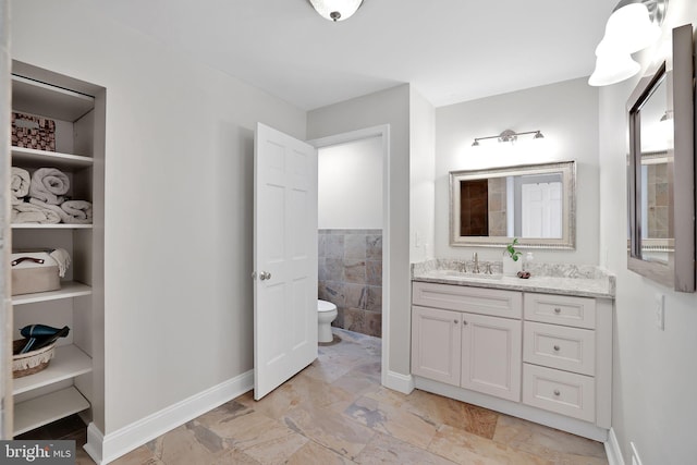 bathroom with toilet, vanity, baseboards, and tile walls