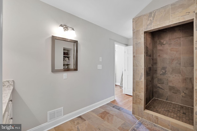 bathroom with tiled shower, baseboards, vanity, and vaulted ceiling
