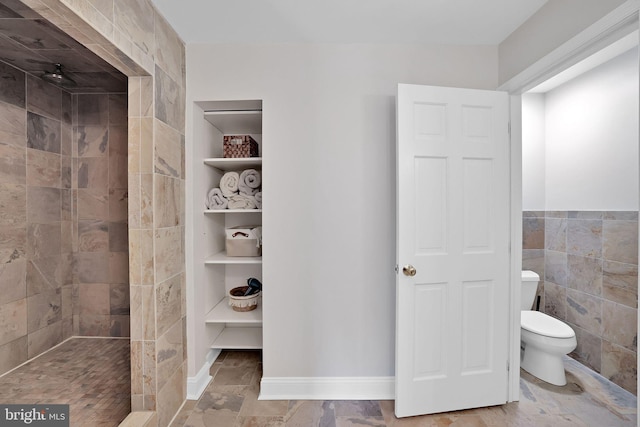 bathroom with a tile shower, built in features, toilet, and tile walls