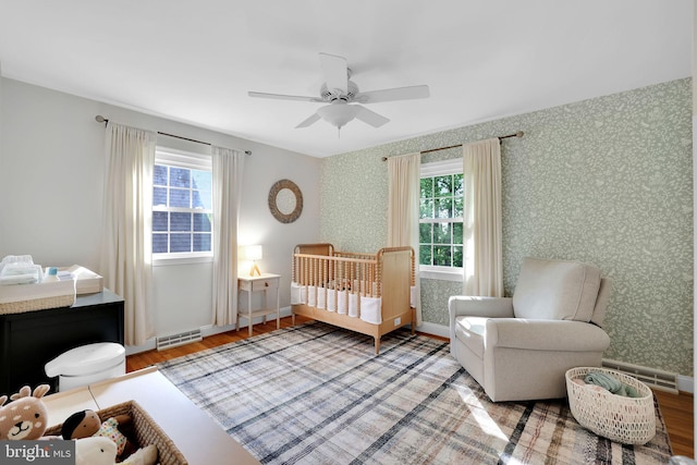 bedroom featuring wood finished floors, multiple windows, wallpapered walls, baseboards, and ceiling fan