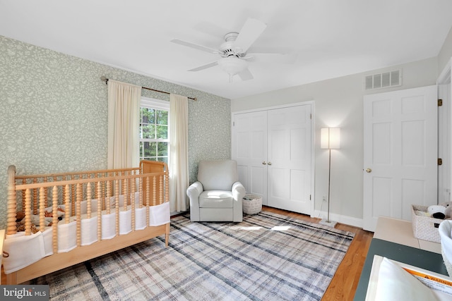 bedroom featuring wallpapered walls, wood finished floors, a closet, and a ceiling fan
