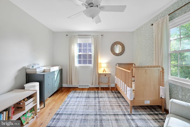 bedroom featuring multiple windows, light wood finished floors, wallpapered walls, baseboards, and ceiling fan