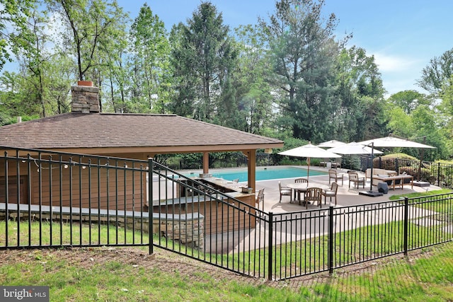 view of pool with a patio, fence, and view of wooded area