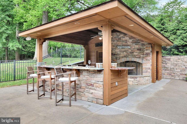 view of patio / terrace with an outdoor stone fireplace, fence, and ceiling fan
