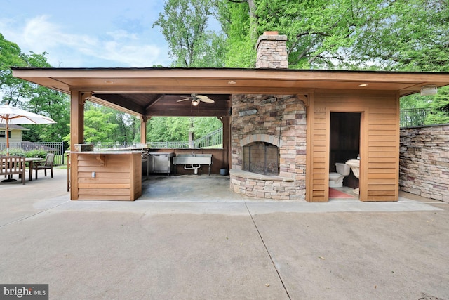 view of patio featuring an outdoor stone fireplace, fence, ceiling fan, and a sink