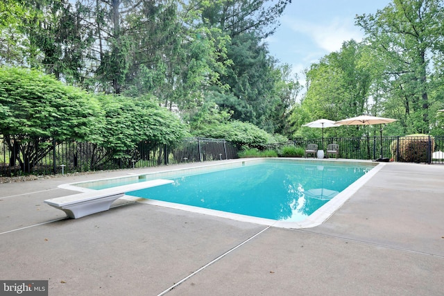 view of swimming pool featuring fence, a diving board, a patio area, and view of wooded area