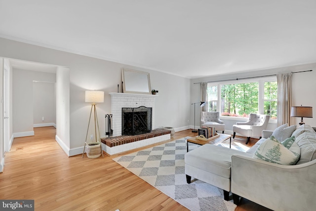 living room featuring a brick fireplace, light wood-type flooring, crown molding, and baseboards
