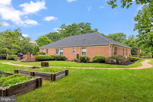 back of house featuring a vegetable garden, brick siding, a yard, and a shingled roof